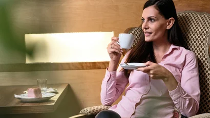 Frau entspannt mit Kaffee und Kuchen in einem gemütlichen Stuhl im Café