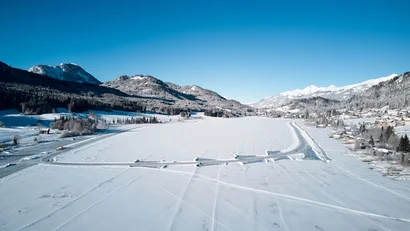 Schneebedeckter See mit geräumten Wegen und Bergen im Hintergrund