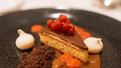 Dessertkuchen mit Schokoladenhaube, roten Beeren, Baiser und Sauce auf schwarzem Teller