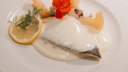 Fischfilet mit cremiger Sauce, Zitronenscheibe, Dill und orangefarbener Blüte