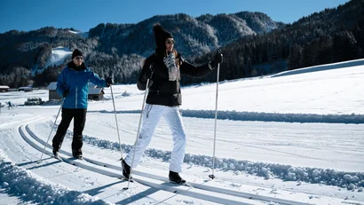 Zwei Personen beim Langlaufen im verschneiten Berggebiet an einem sonnigen Tag