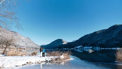 Winterlandschaft mit zugefrorenem See und zwei Personen am Ufer