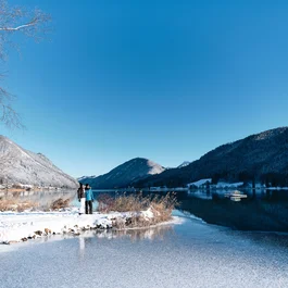 Winterlandschaft mit zugefrorenem See und zwei Personen am Ufer