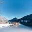 Winterlandschaft mit zugefrorenem See und zwei Personen am Ufer