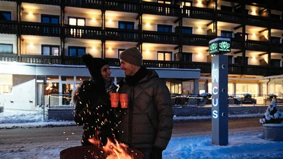 Paar trinkt am Lagerfeuer bei einem beleuchteten Hotel im Winterabend