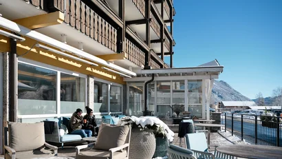 Winterterrasse eines Hotels mit verschneiten Tischen und zwei Personen beim Trinken